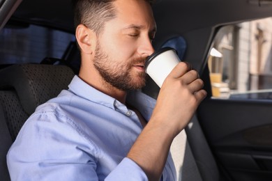 Photo of To-go drink. Handsome man drinking coffee in car
