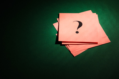 Photo of Pink paper cards with question mark on dark green background, above view. Space for text