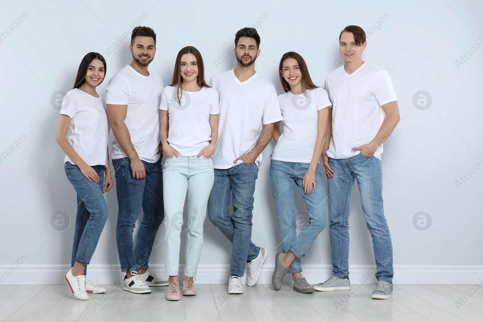 Photo of Group of young people in stylish jeans near light wall