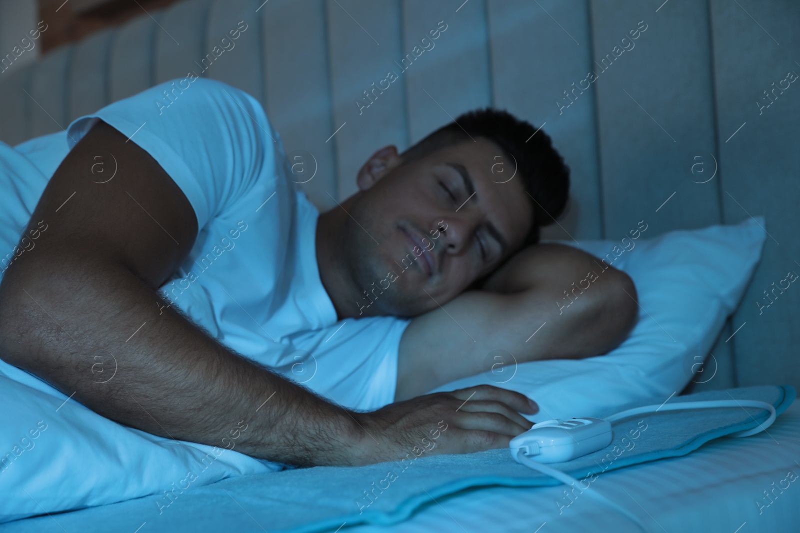 Photo of Man sleeping on electric heating pad in bed at night