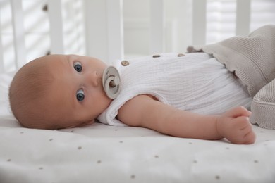 Photo of Cute little baby with pacifier lying on bed