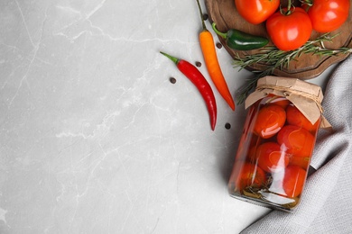 Flat lay composition with pickled tomatoes in glass jar on grey table, space for text