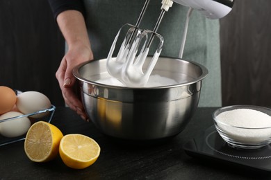 Woman making whipped cream with hand mixer at black table, closeup