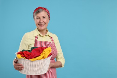 Photo of Happy housewife with basket full of laundry on light blue background, space for text