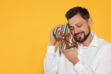 Photo of Happy man with gift box on yellow background, space for text