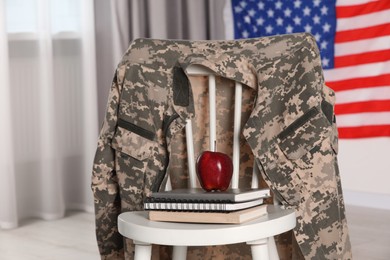 Photo of Chair with soldier uniform, notebooks and apple near flag of United States indoors. Military education
