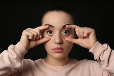 Photo of Woman checking her health condition on black background. Yellow eyes as symptom of problems with liver