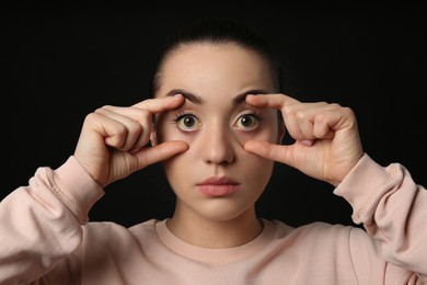 Woman checking her health condition on black background. Yellow eyes as symptom of problems with liver