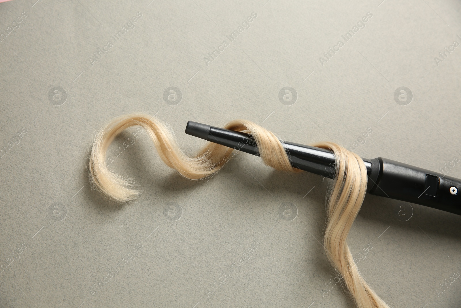 Photo of Modern clipless curling iron and blonde hair lock on grey background, top view