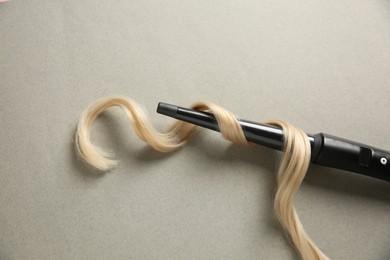 Modern clipless curling iron and blonde hair lock on grey background, top view