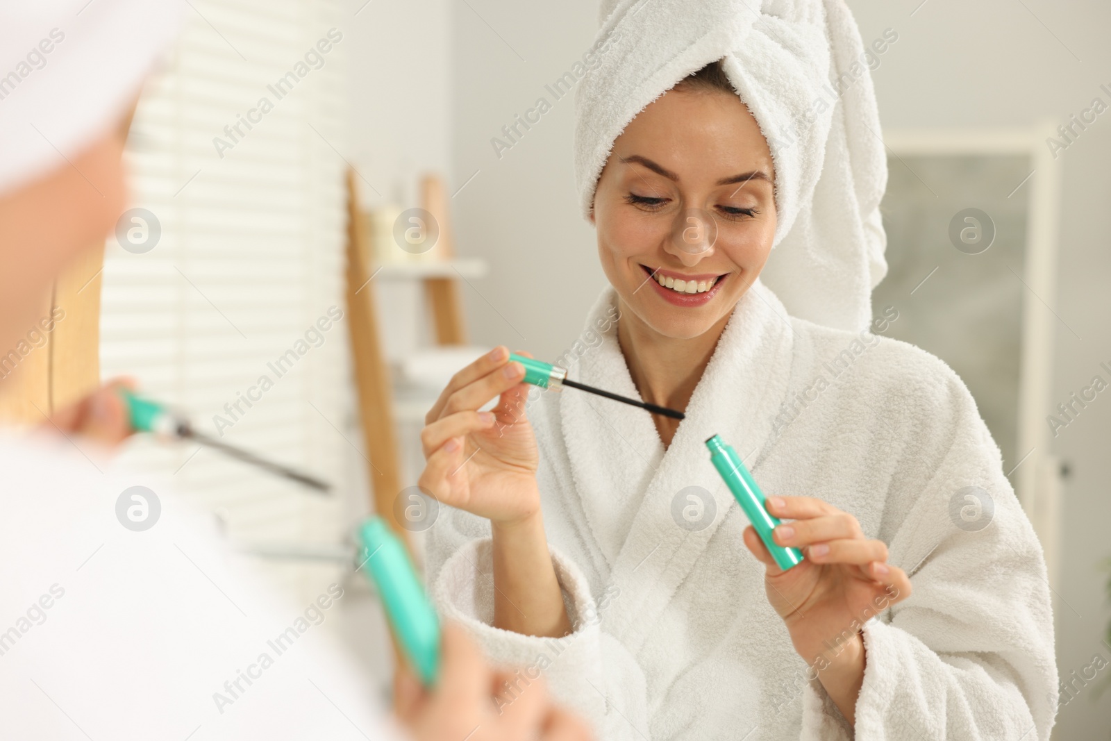 Photo of Beautiful woman with mascara near mirror in bathroom