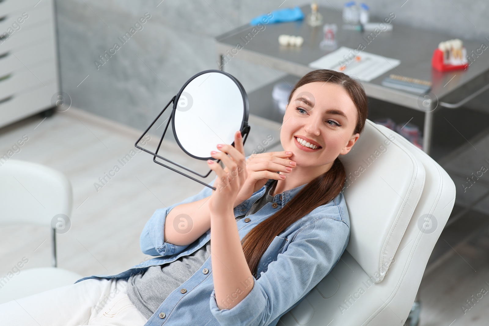 Photo of Young woman looking at her new dental implants in mirror indoors