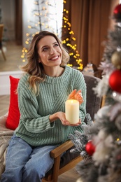 Photo of Young woman with candle near Christmas tree at home