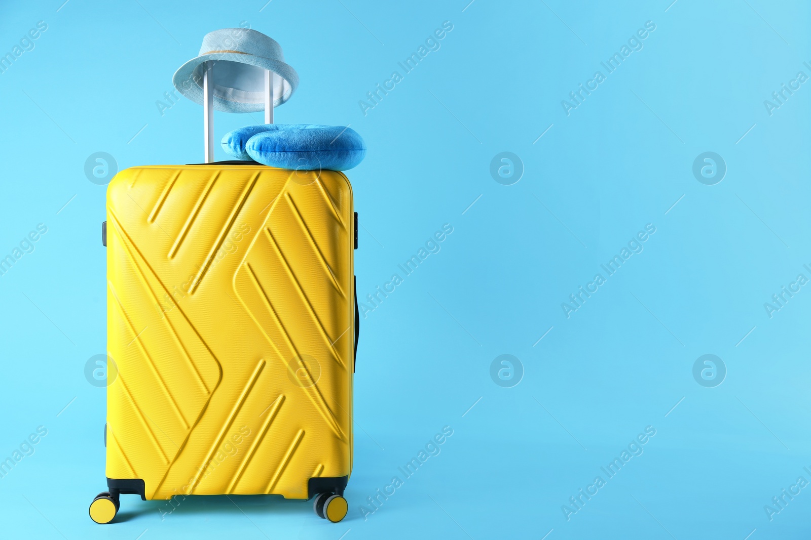 Photo of Yellow suitcase, hat and travel pillow on light blue background, space for text