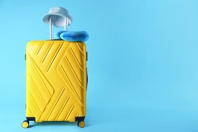 Yellow suitcase, hat and travel pillow on light blue background, space for text