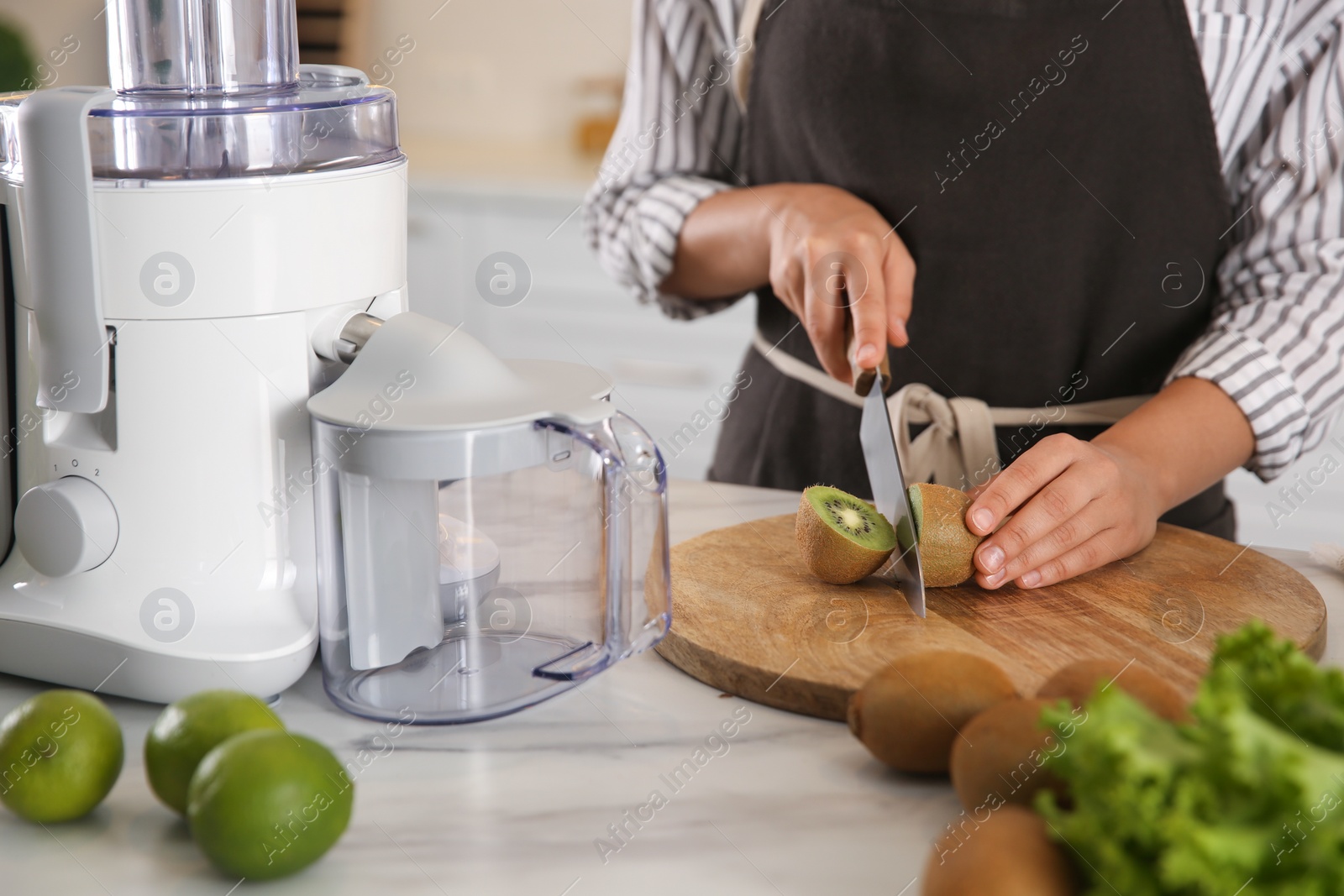 Photo of Young woman cutting fresh kiwi for juice at table in kitchen, closeup