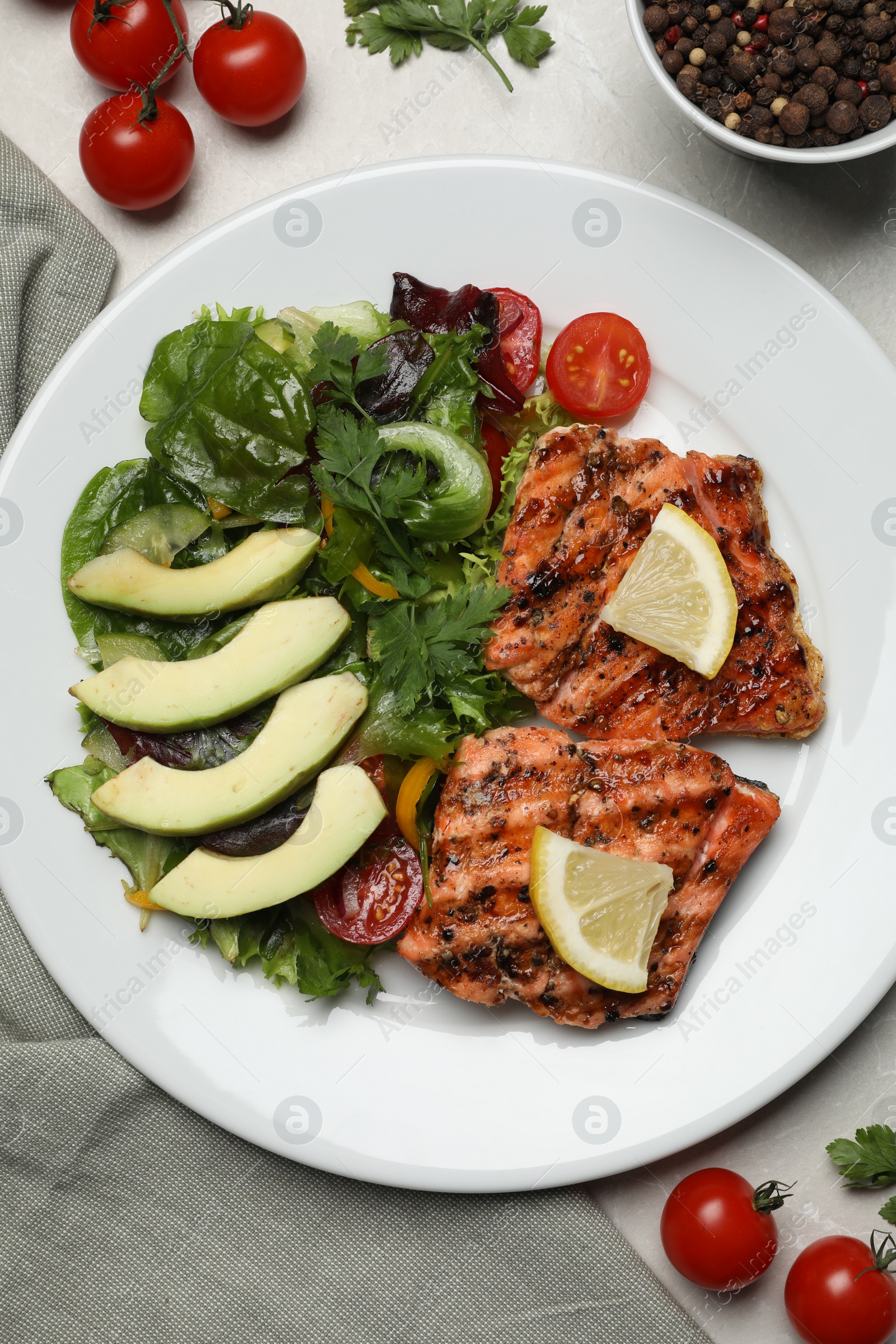 Photo of Tasty grilled salmon with avocado, lemon and tomatoes on light grey table, flat lay