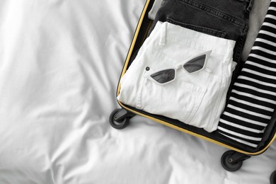 Photo of Open suitcase with clothes and sunglasses on bed, top view. Space for text