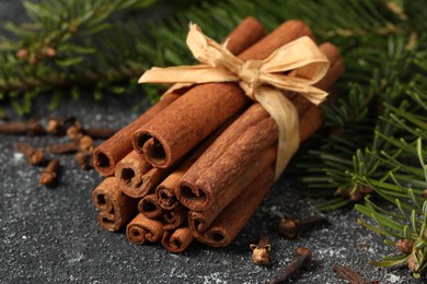 Photo of Different spices. Aromatic cinnamon sticks, clove seeds and fir branches on dark gray textured table, closeup