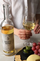 Woman holding glass of white wine at table with snacks, closeup