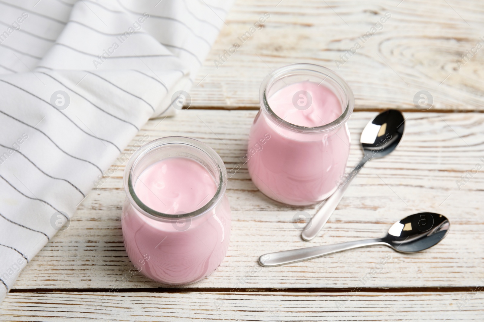 Photo of Glass jars with creamy yogurt served on white wooden table