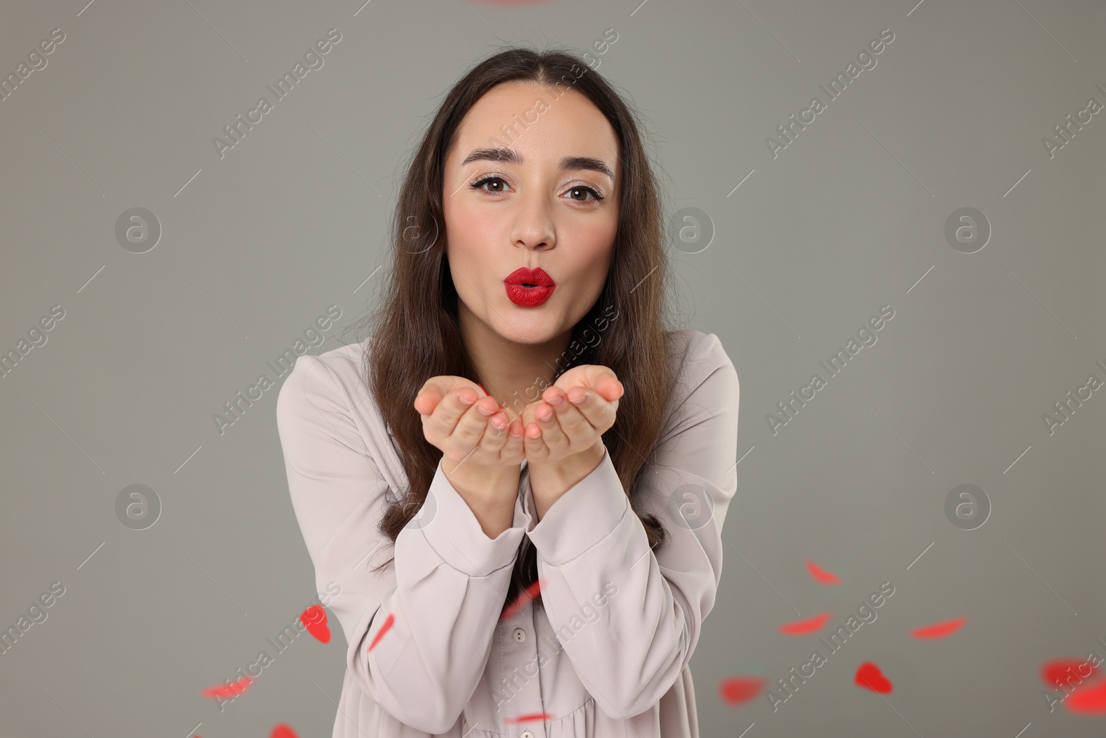 Photo of Beautiful young woman blowing kiss near heart shaped confetti on grey background