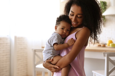 Photo of African-American woman with her baby in kitchen. Happiness of motherhood