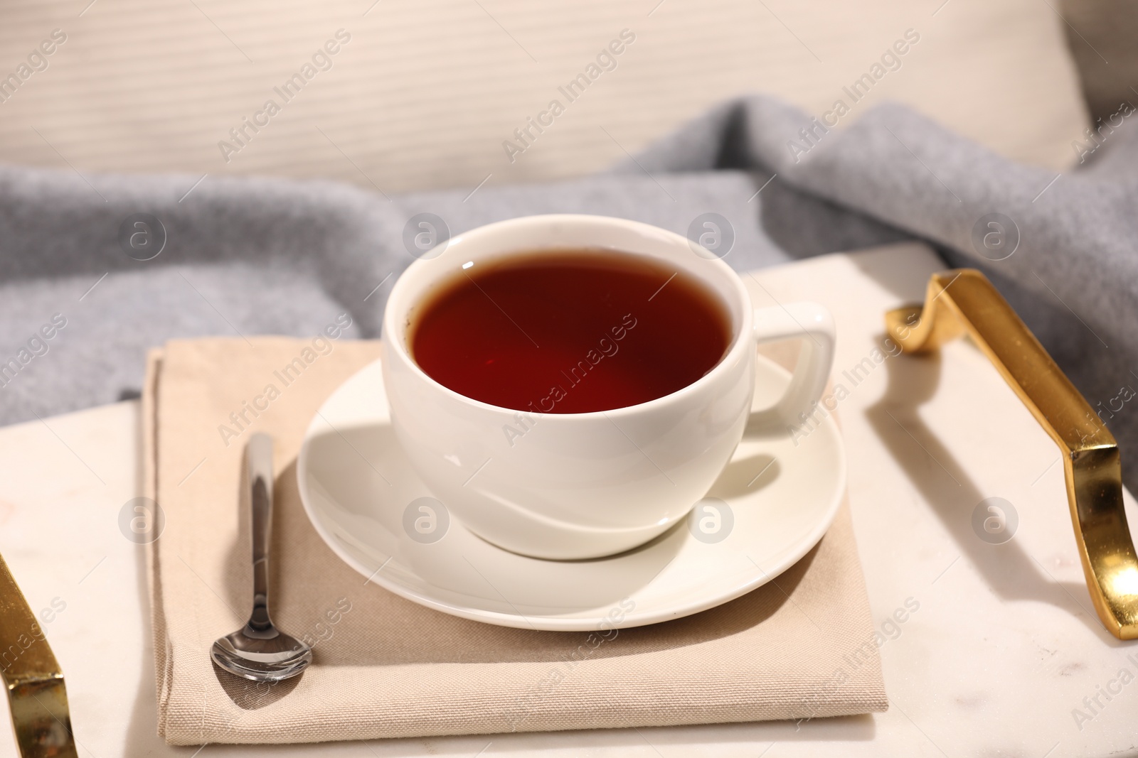 Photo of Aromatic tea in cup, saucer and spoon on bed