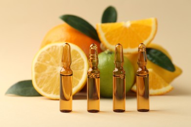 Skincare ampoules with vitamin C, different citrus fruits and leaves on beige background