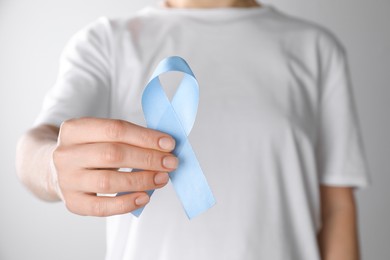 Photo of International Psoriasis Day. Woman with light blue ribbon as symbol of support on white background, closeup
