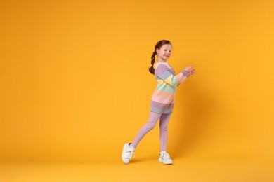 Photo of Cute little girl dancing on orange background