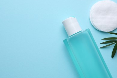 Photo of Micellar water and cotton pad on light blue background, flat lay. Space for text