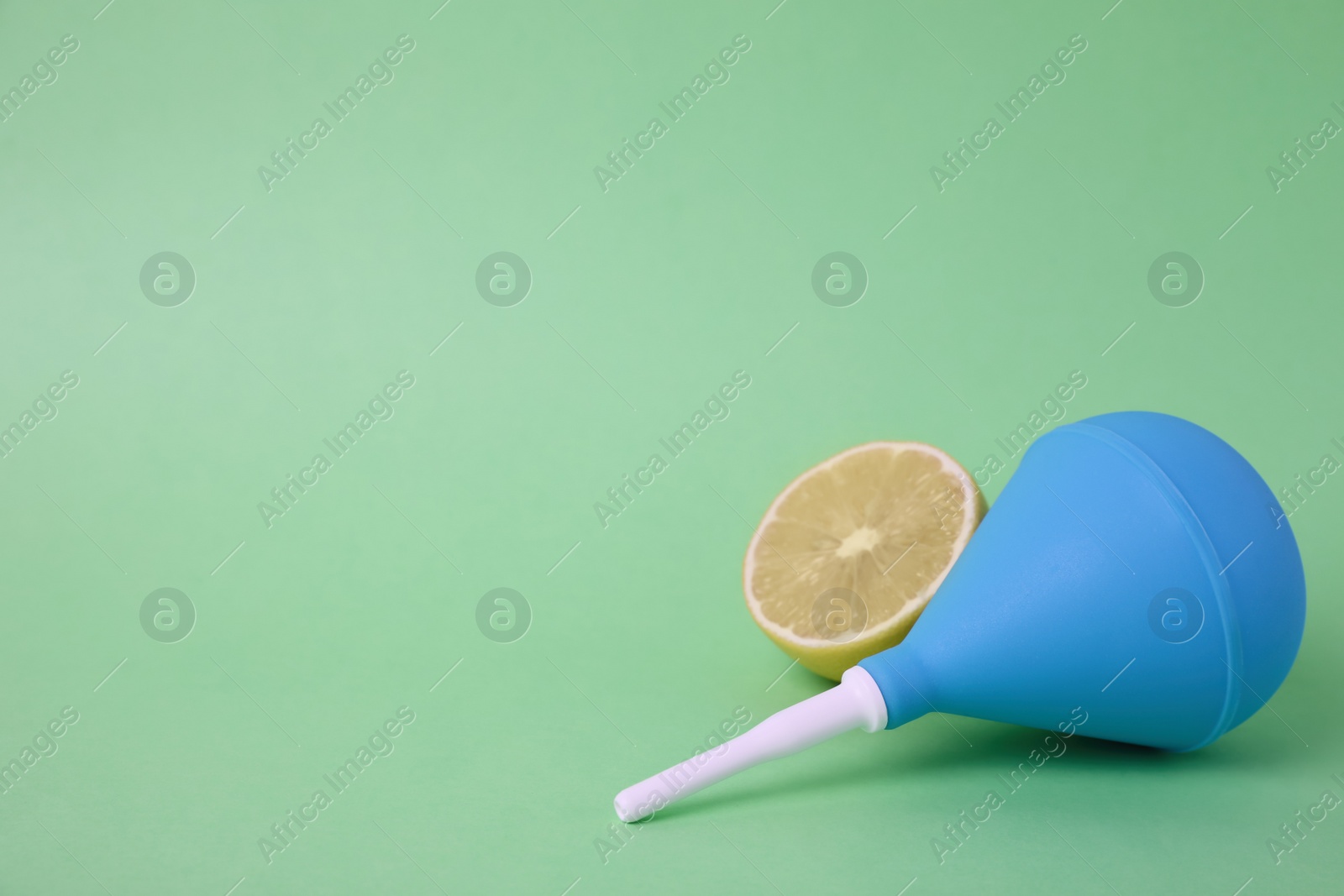 Photo of Enema and half of lemon on green background, space for text. Medical treatment