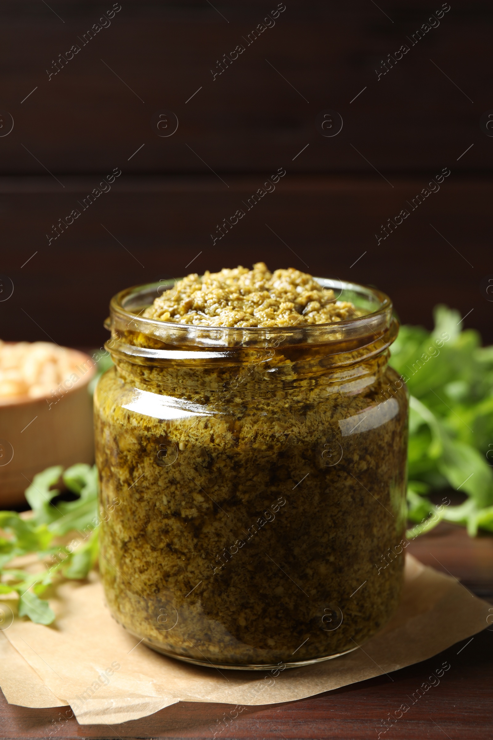 Photo of Jar of tasty arugula pesto on wooden table