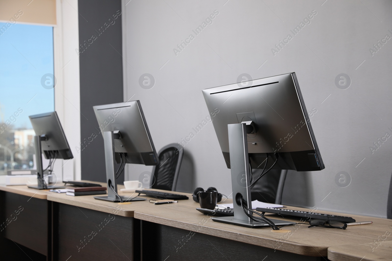 Photo of Open office interior. Modern workplaces with computers near light grey wall