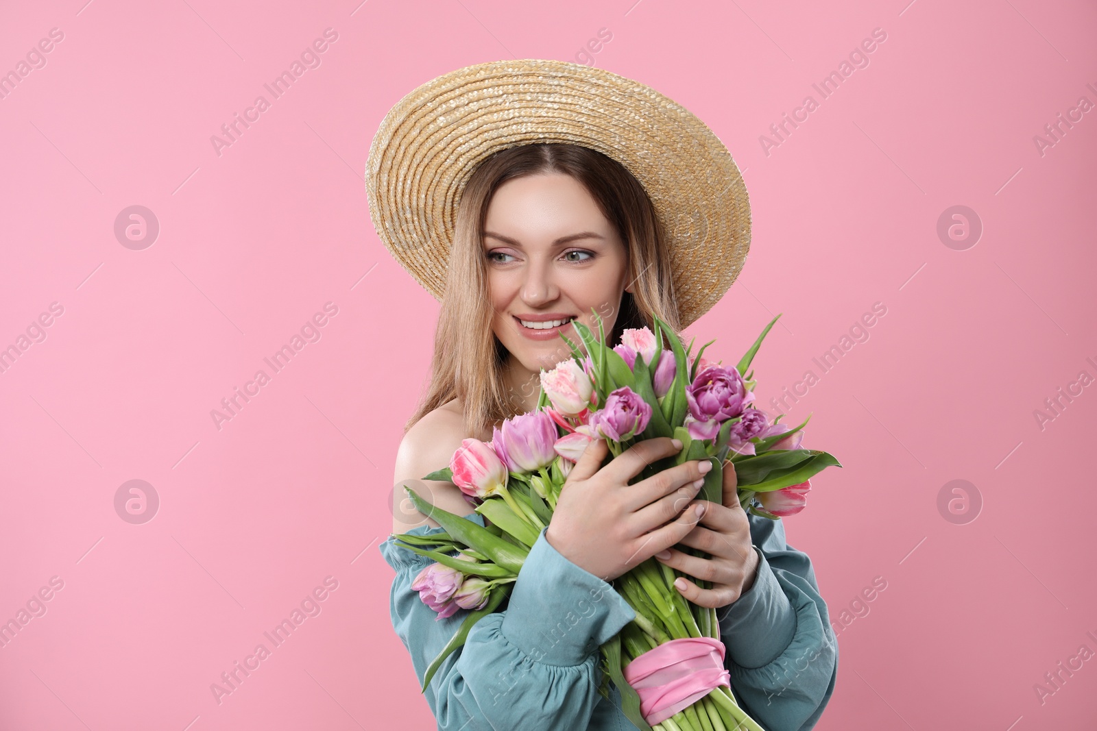 Photo of Happy young woman in straw hat holding bouquet of beautiful tulips on pink background