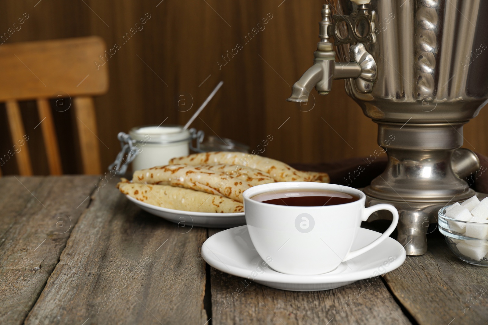 Photo of Vintage samovar, cup of hot drink and pancakes served on wooden table. Traditional Russian tea ceremony