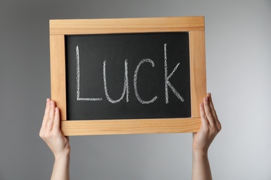 Photo of Woman holding blackboard with word LUCK on light grey background, closeup