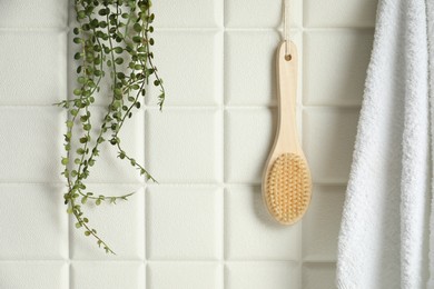 Photo of Bath accessories. Bamboo brush, terry towel and green plant on white tiled wall