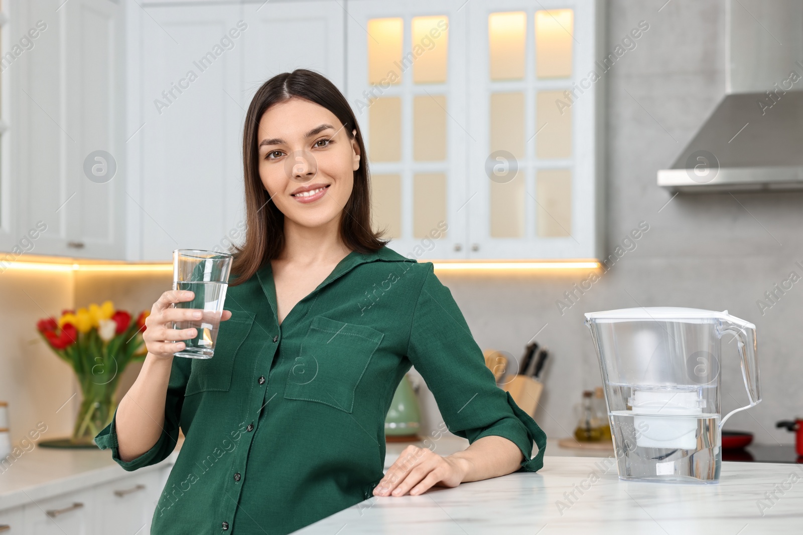 Photo of Woman with glass of water and filter jug in kitchen