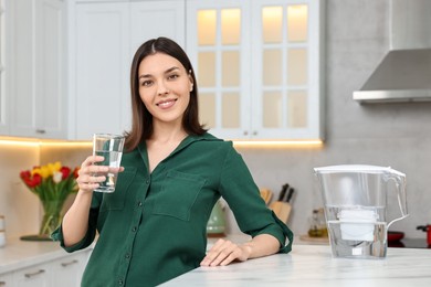 Woman with glass of water and filter jug in kitchen