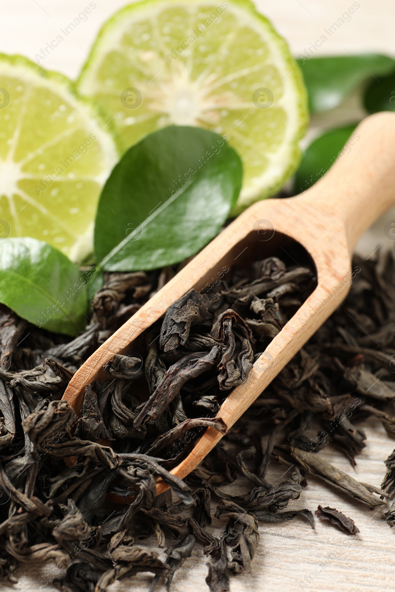 Photo of Dry bergamot tea leaves, wooden scoop and fresh fruit on table, closeup