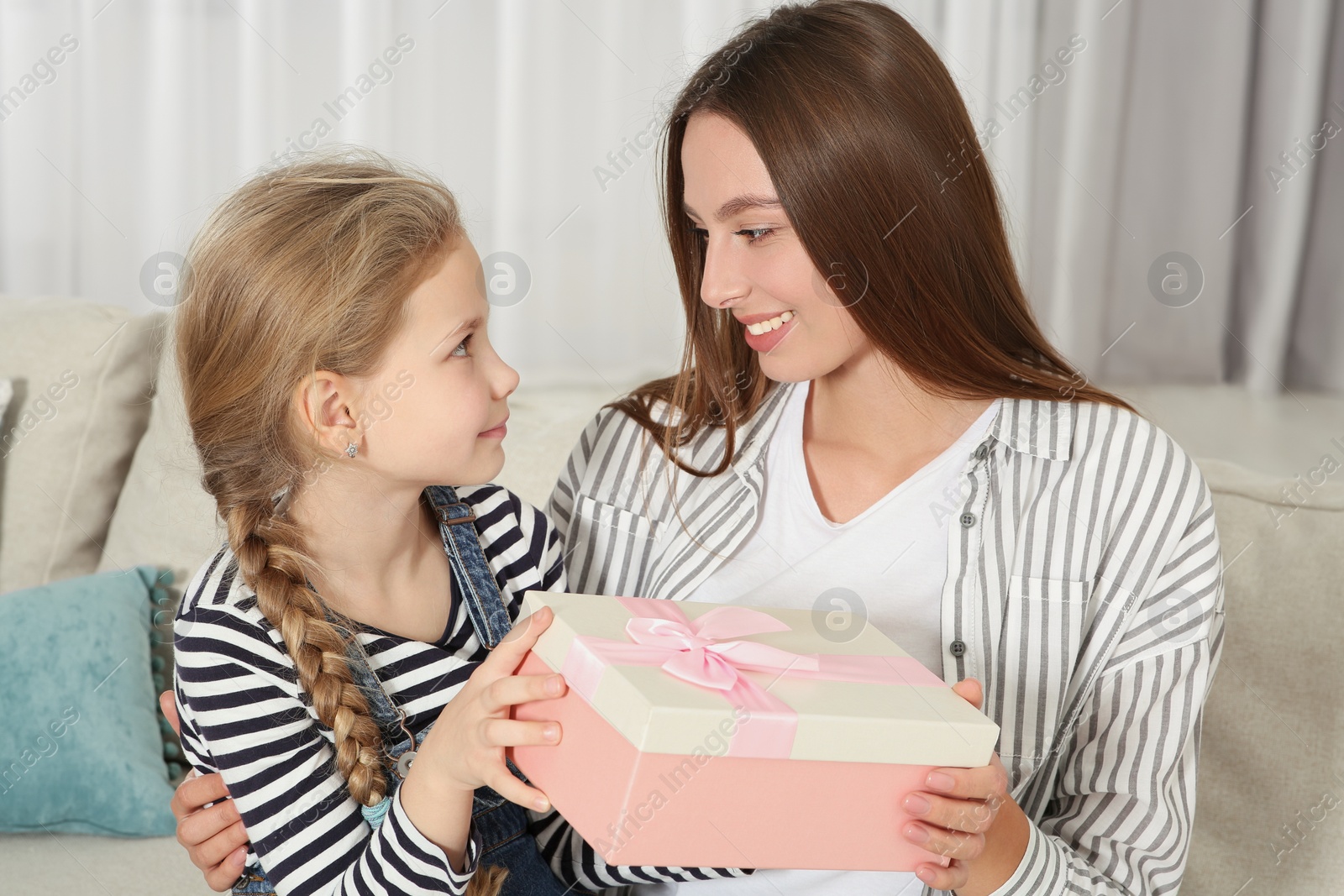 Photo of Cute little girl presenting her mother with gift on sofa at home