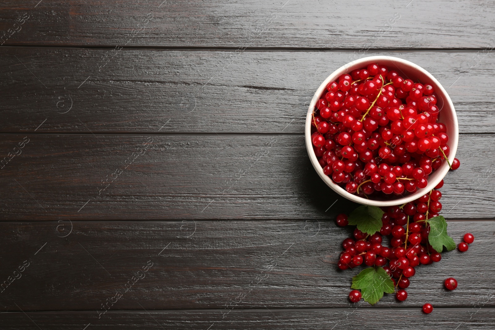 Photo of Delicious red currants and leaves on dark wooden table, flat lay. Space for text