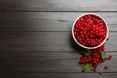 Delicious red currants and leaves on dark wooden table, flat lay. Space for text