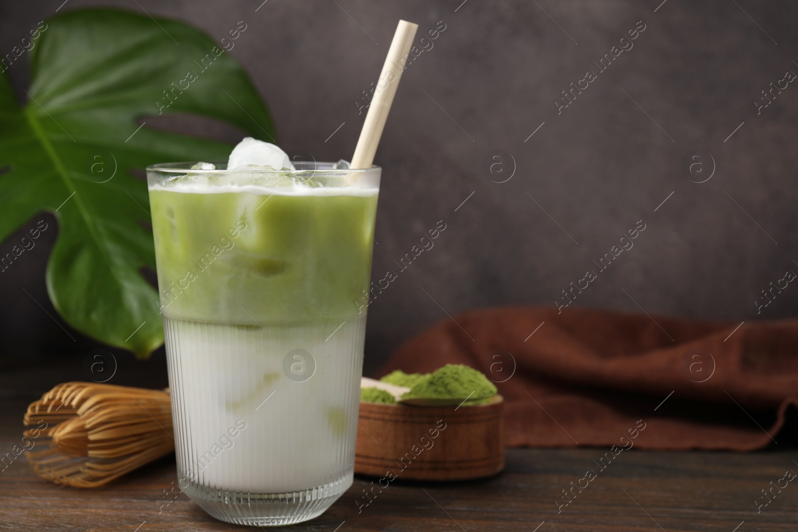 Photo of Glass of tasty iced matcha latte, bamboo whisk and powder on wooden table. Space for text