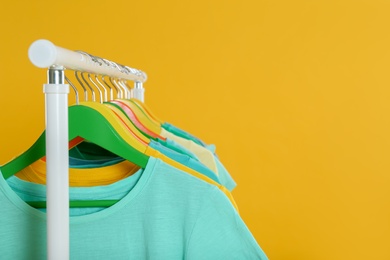Rack with stylish children clothes on yellow background, closeup. Space for text