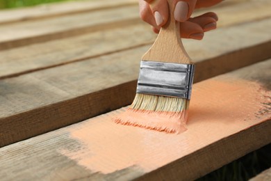 Photo of Woman painting wooden surface with coral dye, closeup