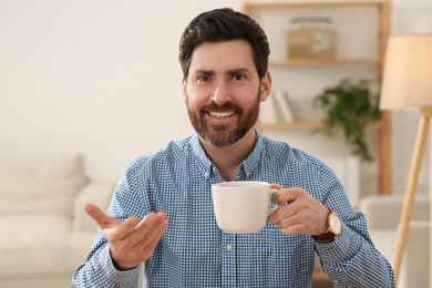 Happy man with cup of drink having video call at home, view from web camera