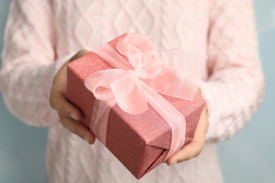 Woman holding beautiful Christmas gift on light blue background, closeup